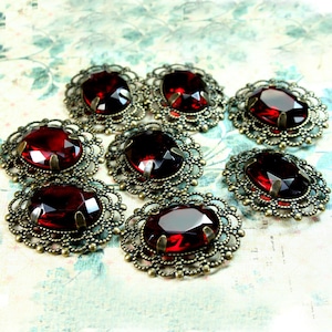 May include: Eight antique-style red glass cabochons with ornate brass settings. Each cabochon is set in a filigree design with a scalloped edge.