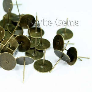 May include: A pile of antique brass earring blanks. The blanks are round with a small hole in the center and a post attached to the back.