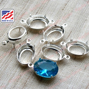 May include: Six silver oval-shaped bezel settings with prongs and a loop for hanging. One setting is filled with a light blue gemstone.