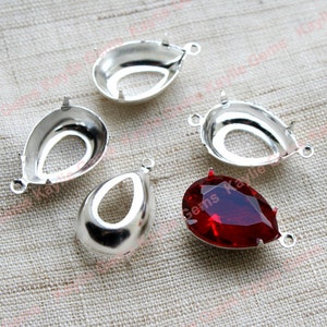 May include: Five silver-toned metal settings for attaching a teardrop-shaped gem or rhinestone. One setting is filled with a red teardrop-shaped gem.