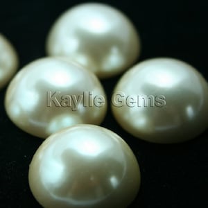 May include: Close-up of five off-white pearl cabochons, each with a smooth, rounded surface. The pearls are arranged in a semi-circle on a black background. The text "Kaylie Gems" is visible in the centre of the image.