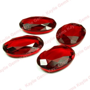 May include: Four red oval-shaped faceted glass gems on a white background.