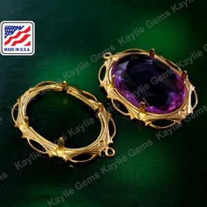May include: Two gold-tone metal settings for a large oval-shaped gemstone. The settings have a decorative, ornate design. One setting has a purple gemstone in place.