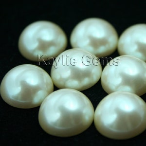 May include: A group of eight off-white pearl-like round cabochon gems on a black background.