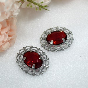 May include: Two red glass oval-shaped cabochons set in silver filigree frames. The frames have a delicate, intricate design.