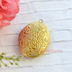 May include: Gold oval locket with an ornate floral design. The locket has a hinged opening and a loop for attaching a chain.