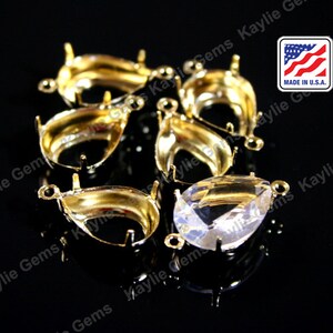 May include: A collection of gold-colored, teardrop-shaped jewelry settings with small loops and prongs. One setting holds a clear, pear-cut gemstone. The image includes a small "MADE IN U.S.A." label.