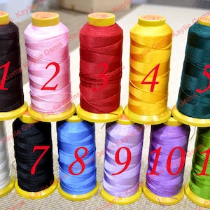May include: Eleven spools of thread in various colors, including black, white, pink, red, yellow, green, blue, and purple. Each spool is numbered 1 through 11.