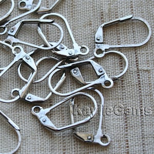 May include: A pile of silver-toned earring hooks, also known as leverback earring findings. These are metal earring closures that attach to the back of earrings.