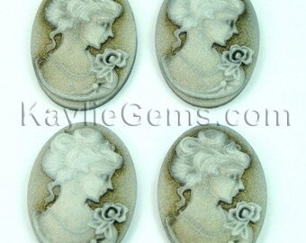 May include: Four oval-shaped cameo pendants with a raised design of a woman's profile with a flower. The cameo is white with a light brown background.
