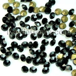 May include: A close-up image of black and gold rhinestones. The rhinestones are scattered on a white surface.