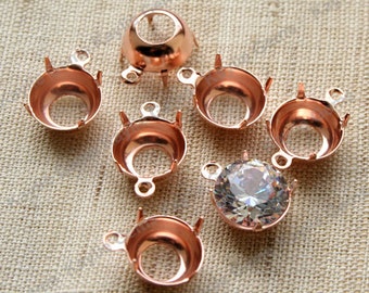 Könnte beinhalten: Ein Satz mit acht roségoldfarbenen Metallfassungen zum Befestigen von Strasssteinen oder anderen Verzierungen. Die Fassungen haben eine runde, offene Oberseite und drei Zinken an der Unterseite. Eine Fassung hat einen klaren Strassstein, der bereits befestigt ist.