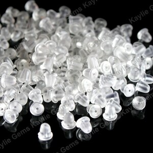 May include: A large pile of clear plastic earring backs. The backs are small and round with a small hole in the center.