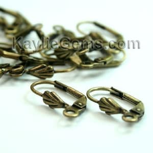 Puede incluir: Primer plano de un montón de hallazgos de pendientes de color dorado antiguo con un diseño festoneado. Los hallazgos son de metal y tienen un cierre de gancho.