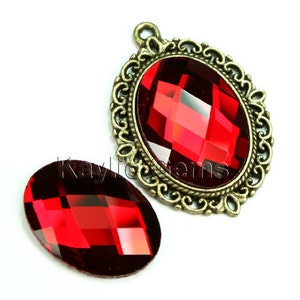 May include: Two red faceted glass cabochons, one set in an ornate antique gold-toned metal frame. The larger cabochon is approximately 2 inches in diameter.