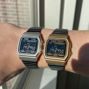 May include: Two Casio F-91W digital watches with black bands. The watch on the left has a silver case and the watch on the right has a gold case. Both watches display the time 14:24:50.
