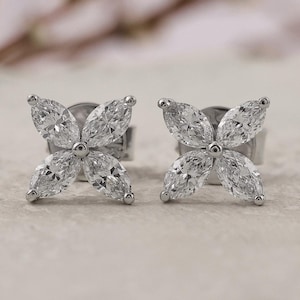 Op de afbeelding: Een paar zilveren oorstekers, elk met een vierbladige bloemvorm. Elk bloemblad is samengesteld uit een marquise-geslepen, heldere edelsteen. De oorbellen zijn geplaatst tegen een neutrale achtergrond met zachte, vage bloemaccenten.