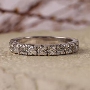 May include: A silver-toned eternity band ring featuring a continuous row of small, round, clear faceted stones set in a channel or shared-prong style. The metal band has a polished finish and reflects light across the circular surface.