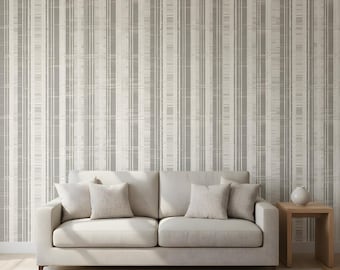 May include: A neutral-toned living room scene featuring a light-colored sofa with several throw pillows. The backdrop is a gray and white striped wallpaper. A small wooden side table holds a white vase, and a rug is on the floor.
