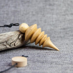 May include: A wooden pendulum with a spiral design and a black cord. The pendulum is made of light wood and has a natural finish.