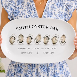 May include: An oval white serving platter with the text "SMITH OYSTER BAR" and an illustration of six oysters. Below the text are the words "SOLOMONS ISLAND MARYLAND" and coordinates. The platter is held by a person wearing a blue and white floral dress.