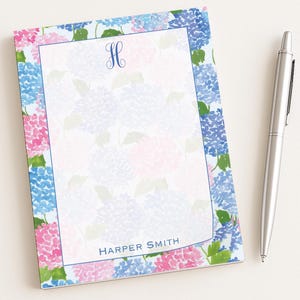 Könnte beinhalten: Ein rechteckiger Notizblock mit einem Aquarell-Hortensien-Blumenmuster in Blau-, Rosa- und Grüntönen. Die Mitte hat eine weiße Schreibfläche mit blauem Rand, ein blaues H-Monogramm oben und den Text HARPER SMITH am unteren Rand.