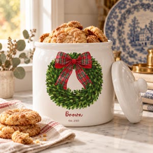Peut inclure: Un pot à biscuits en céramique blanche orné d'une couronne verte avec un nœud écossais rouge. Le texte "Brown" et "Est. 2025" est imprimé en rouge sous la couronne. Le pot a un couvercle blanc assorti et contient des biscuits.