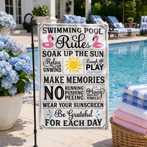 May include: A white rectangular garden flag with black text that reads "Swimming Pool Rules." The flag features pink flamingo floaties, a yellow sun, and other pool-related phrases. The flag is displayed outdoors near a pool.
