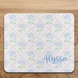 May include: A rectangular mouse pad featuring a white background with a repeating pattern of light blue hydrangea flowers and soft pink diagonal lattice lines. The name Alyssa is printed in a blue script font in the bottom right corner.