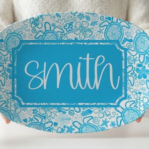 May include: An oval serving platter featuring a blue and white pattern of sea turtles, hibiscus flowers, and starfish. A central rectangular frame with a solid blue background contains the white cursive text "smith" in the middle of the platter.