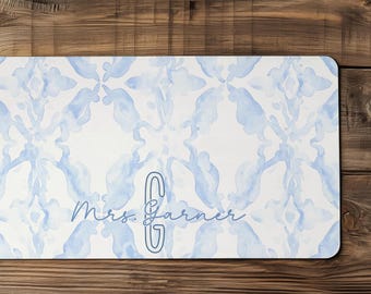 May include: A rectangular desk mat featuring a light blue and white watercolor pattern with a repeating abstract motif. The center displays the text Mrs. Garner in a script font alongside a large, stylized capital letter G in a dark blue outline.