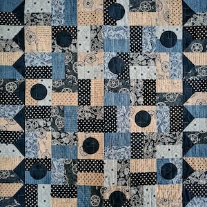 May include: A patchwork quilt with a geometric design. The quilt features squares and triangles in various patterns, including polka dots, floral prints, and solid colors. The color palette includes navy blue, light blue, beige, and black. The quilt has a circular design in the center of some squares.