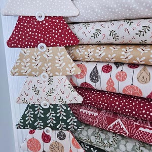 May include: A vertical fabric wall hanging featuring a stack of trapezoidal fabric segments connected by white buttons. The segments display various holiday-themed patterns including candy canes, berries, ornaments, and houses in red, green, and cream.