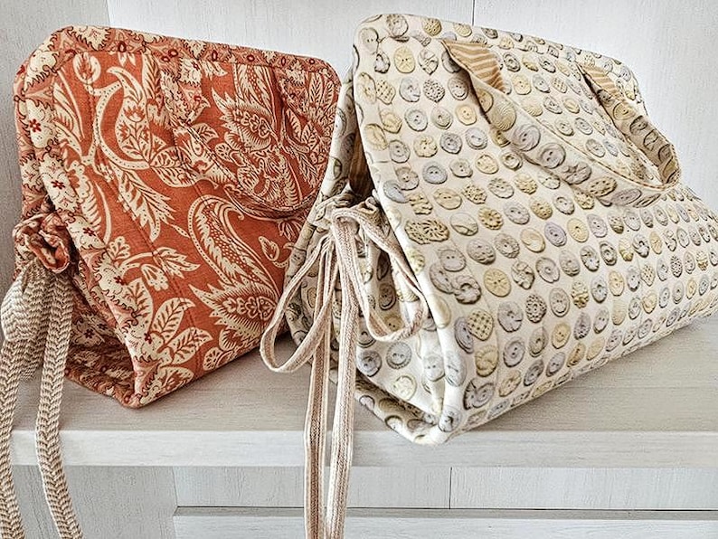 May include: Two fabric bags with drawstring closures. One bag features a rust-colored paisley pattern, while the other displays a pattern of various buttons. Both bags have matching fabric handles and drawstrings.