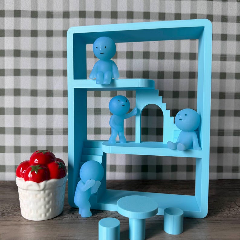 K&ouml;nnte beinhalten: Eine hellblaue Miniatur-Architekturstruktur mit kleinen Figuren, einem Tisch und zwei Hockern. Die Struktur hat mehrere Ebenen mit kleinen blauen Figuren in verschiedenen Posen. Eine wei&szlig;e Keramikschale mit roten Tomaten befindet sich links.