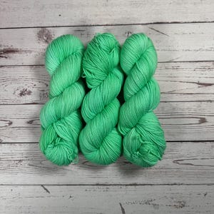 Puede incluir: Tres ovillos de hilo verde brillante, retorcidos juntos.