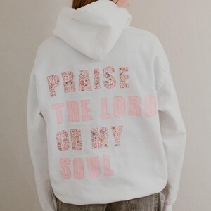 May include: White hoodie with a pink floral design on the back that says "Praise the Lord oh my soul".