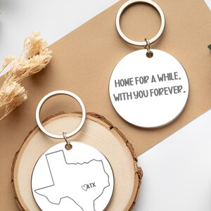 Puede incluir: Dos llaveros plateados con anillos dorados. Uno presenta el contorno de Texas con "ATX" y un corazón. El otro llavero tiene el texto "HOME FOR A WHILE, WITH YOU FOREVER."