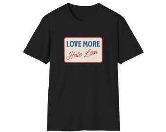 May include: Black t-shirt with a rectangular graphic. The graphic has a blue border and the words "LOVE MORE" in blue, and "Hate Less" in red, on a cream background. The shirt is a classic crew neck style.
