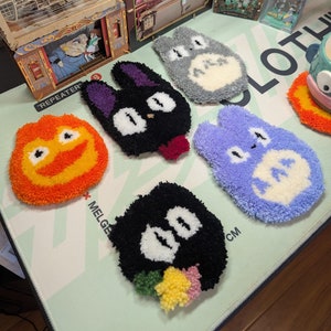 May include: A selection of handmade character coasters in various colours. The coasters depict characters from animated films, including a grey Totoro, a black soot sprite, and a purple Totoro.