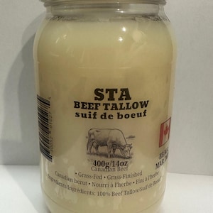 Op de afbeelding: Een doorzichtige pot met een witte deksel gevuld met rundertalg. Het etiket luidt "STA BEEF TALLOW" en "400g/14oz Canadian Beef". De pot bevat ook een tekening van een koe en de Canadese vlag.