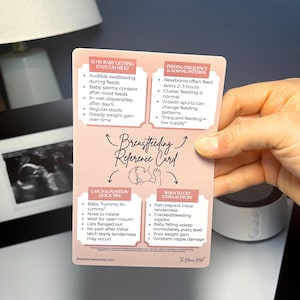 May include: A pink and white breastfeeding reference card held by a hand. The card provides quick tips on latching, feeding frequency, and when to get extra support. The card also includes information on whether the baby is getting enough milk.