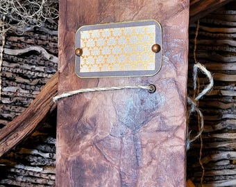 May include: A handmade journal with a textured, brown cover and a decorative label featuring a gold geometric pattern. The journal is bound with twine and has a rustic aesthetic. Decorative blue bird figurines and a nest are in the background.