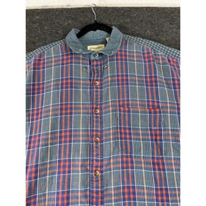 May include: A long-sleeved button-down shirt featuring a plaid pattern in shades of blue, green, and orange. The shirt includes a single chest pocket, a standard collar with a St. Johns Bay label, and brown buttons running down the front placket.