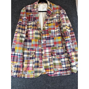 May include: A long-sleeve blazer featuring a patchwork design of various plaid and checkered patterns in red, yellow, blue, green, and white. The garment includes a notched lapel, two front flap pockets, and white buttons on the front and cuffs.