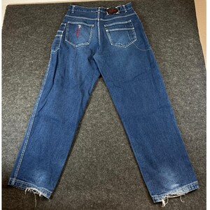 May include: Dark blue denim jeans featuring a high-waisted design with belt loops, two back pockets, and a small utility pocket on the side. The back pockets have red embroidered details, and the leg hems show visible fraying and wear.