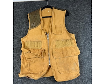 Op de afbeelding: Een beige utility-vest met een ritssluiting aan de voorzijde, meerdere grote opgestikte zakken en een donker olijfgroen gewatteerd schouderstuk aan de rechterkant. Het kledingstuk is gemaakt van stevige stof en bevat een kleine borstzak.