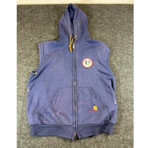May include: A blue sleeveless zip-up hoodie with a hood and drawstring. The front features a circular patch with the text "PLUMBERS & PIPEFITTERS UA LOCAL 1960" and a small Carhartt logo near the bottom pocket. The garment shows signs of wear.