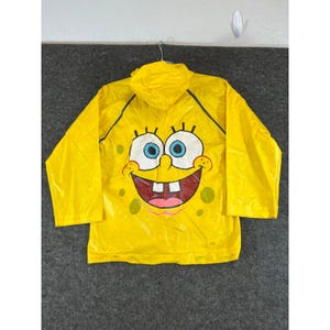 May include: A bright yellow hooded raincoat featuring a large graphic print of the Spongebob Squarepants character face on the back. The design includes two large white eyes with blue irises, a wide smiling mouth with teeth, and scattered green spots.