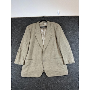 May include: A beige and brown herringbone blazer featuring a notched lapel, two front buttons, and two lower pockets. The jacket is fully lined with a smooth, light-colored interior fabric and is displayed on a black hanger.